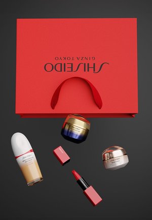 Rode Shiseido cadeautas met handvat toont huidverzorgings- en make-upproducten: een witte essence fles, twee potjes en een lippenstift in rode verpakking.