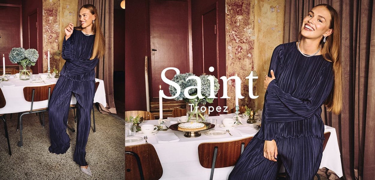 Navy pleated two-piece set featuring a long-sleeve top with ruffled hem and matching trousers, set against an elegant dining backdrop.