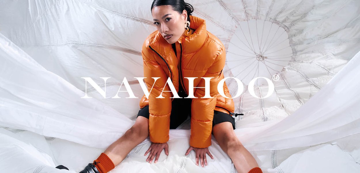 Orange Steppjacke mit hohem Kragen und Reißverschluss, mit glänzender Textur und gesteppten Details, getragen über einem schwarzen Outfit.