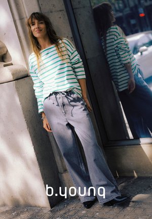 Gestreiftes Langarmshirt in Weiß und Türkis, kombiniert mit hellgrauen, weit geschnittenen Hosen. Glatter Stoff mit entspannter Passform. Reflektiert auf einer Glasoberfläche.