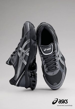 Sorte og grå atletik sko med en overdel i mesh og syntetisk materiale, der har sølvfarvede detaljer og en polstret sål for støtte.