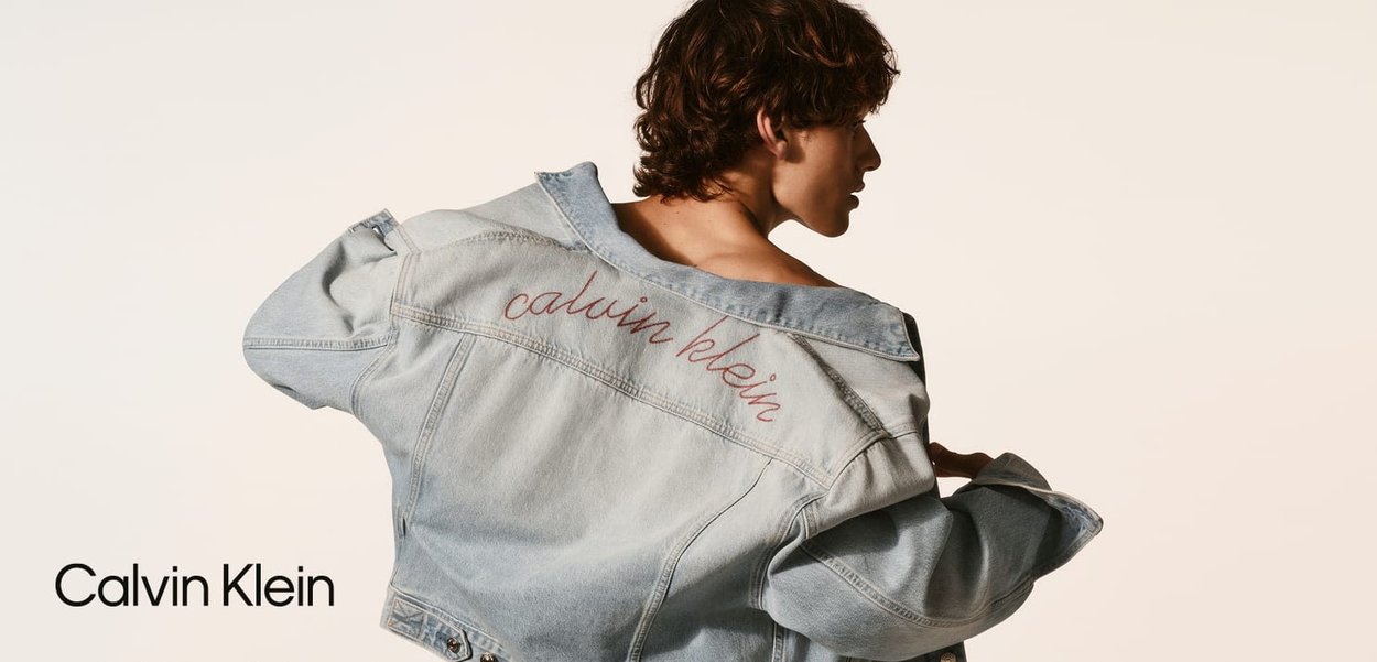 Helle blaue Denimjacke mit oversized Passform, ausgestattet mit gesticktem "calvin klein" in Rot auf dem Rücken. Glatte Textur und klassisches Design.