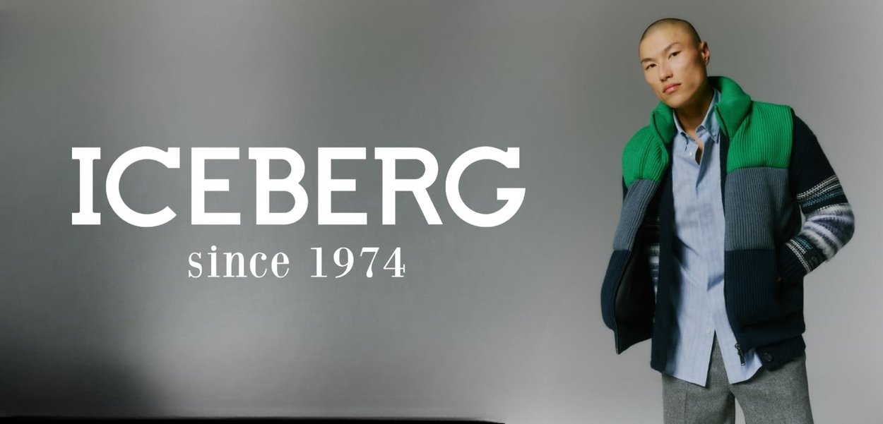 Marineblaue Jacke mit grünem Strickkragen, geschichteten grauen Einsätzen und gestreiften Akzenten, getragen über einem hellblauen Hemd.