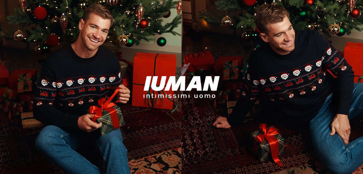 Pull en tricot noir avec motifs festifs, jean bleu et un cadeau. En arrière-plan, un sapin de Noël décoré et des cadeaux emballés.
