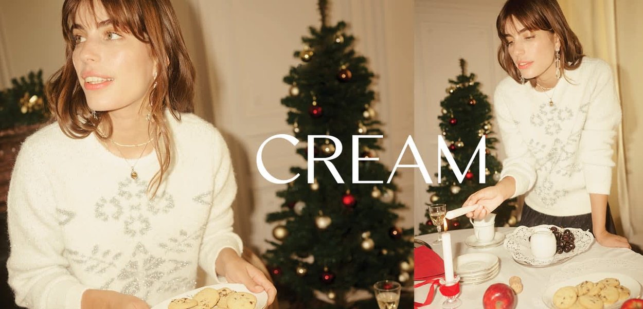 Cremefarbener Strickpullover mit dekorativem grauem Muster, getragen beim Servieren von Keksen auf einem Tisch mit festlicher Dekoration und einem Weihnachtsbaum.