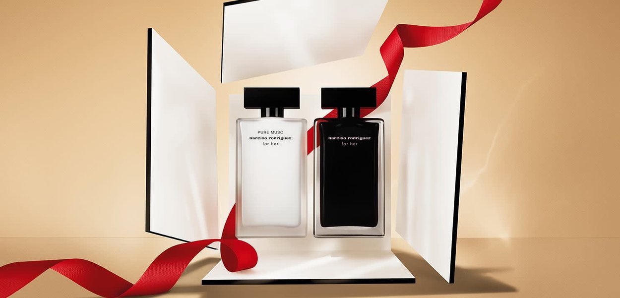 Twee parfumflessen, een doorzichtige met een zwarte dop met het label "PURE MUSC" en een zwarte fles, beide tentoongesteld in een witte doos met een rood lint.