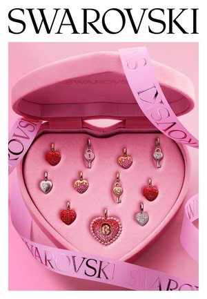 Hartvormige en sleutelvormige Swarovski-bedels in rood, roze en zilver, in een roze hartvormige sieradendoos met roze merkbandjes.