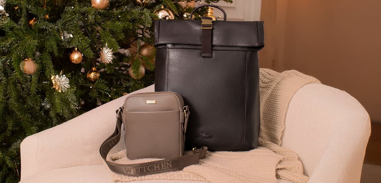 Sac à dos en cuir noir avec fermeture à boucle et sac bandoulière gris avec un logo. Les deux sacs reposent sur un plaid en tricot beige.