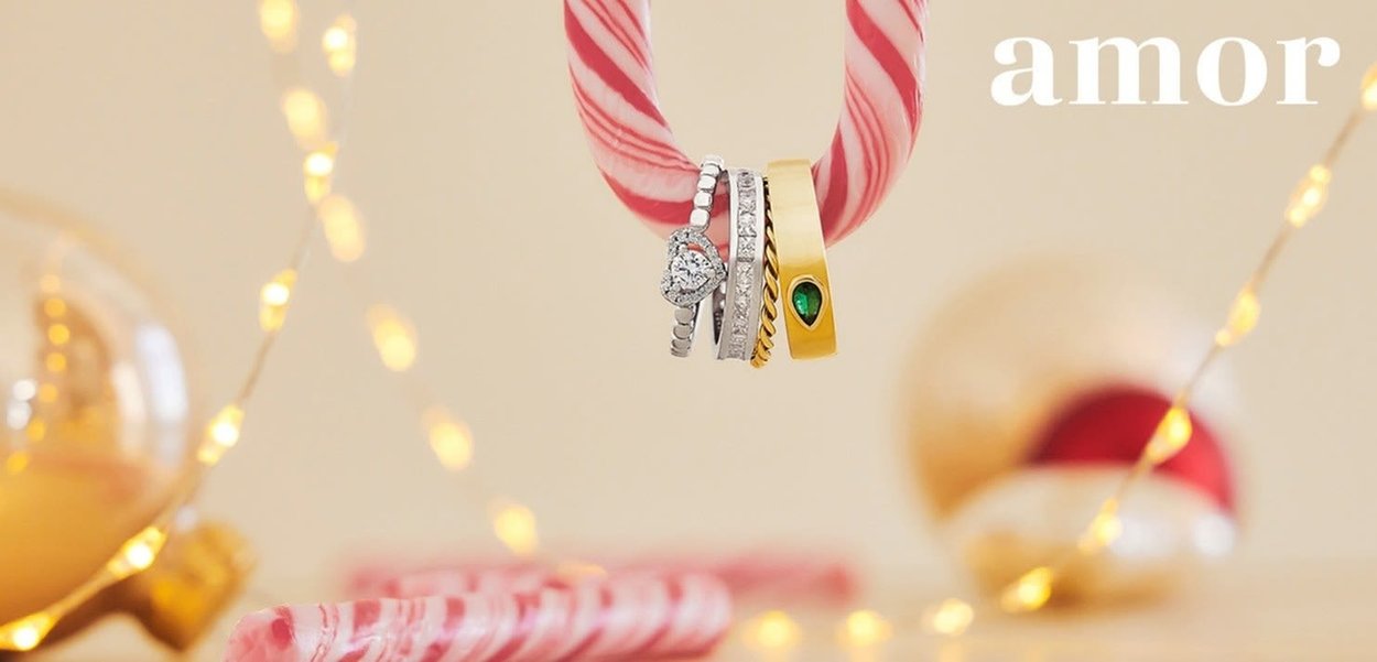 Tre anelli appesi a un nastro rosa e bianco. Comprendono un anello d'oro con una gemma verde, un anello a forma di cuore con diamante e una fede nuziale d'argento.