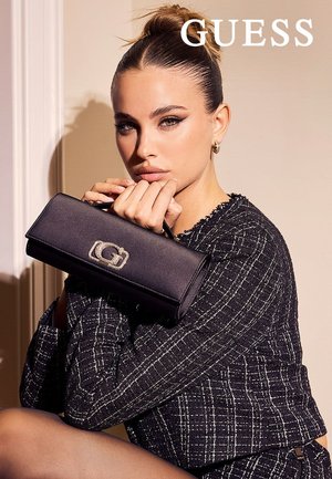 Bolso tipo cartera negro con cierre plateado brillante con la letra "G", sostenido en las manos de una modelo, combinado con un blazer negro texturizado.