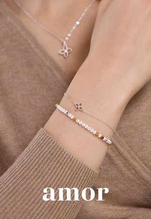 Silberne Armbänder mit einem floralen Charm und Perlenakzenten, die runde Perlen in Braun-, Creme- und Goldtönen aufweisen. Am Handgelenk getragen.
