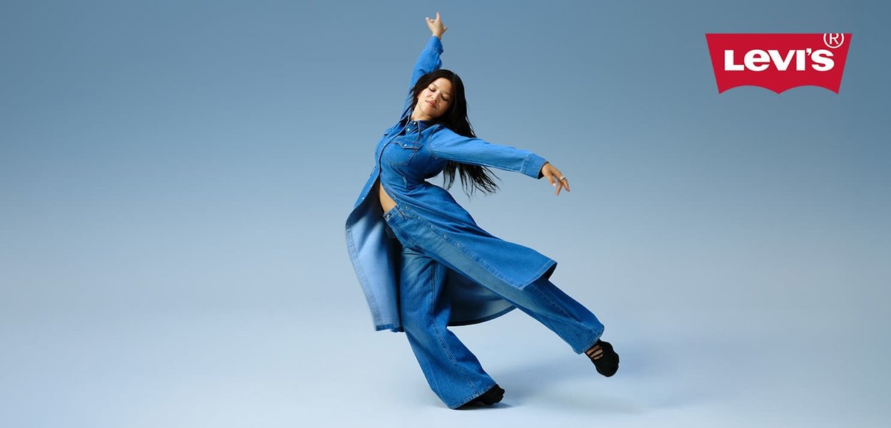 Denim outfit med en lang, blå skjorte og brede, blå jeans. Modellen poserer dynamisk. Baggrunden er en lyseblå gradient. Levi's logo er inkluderet.