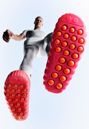 Suole di scarpe da ginnastica di un rosa brillante con accenti circolari arancioni. Il design della scarpa presenta una forma arrotondata e una superficie strutturata, vista dal basso.