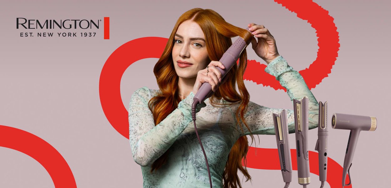 Kvinna med långt rött hår som stylar en sektion med en rosa värmeborste, med tre andra rosa hårstylingsverktyg visade i närheten.