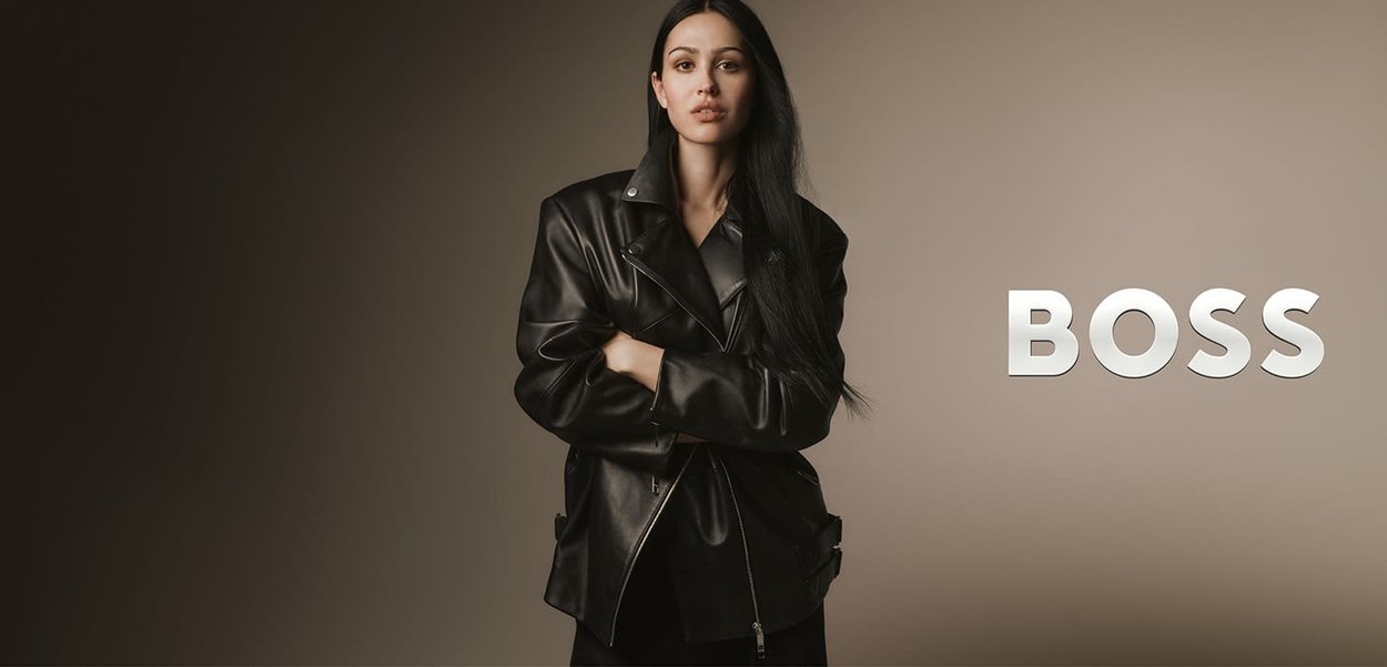Chaqueta de cuero negro con un diseño estructurado, que presenta un frente de doble botonadura, herrajes plateados y un ajuste relajado. Texto de marca en el lateral.