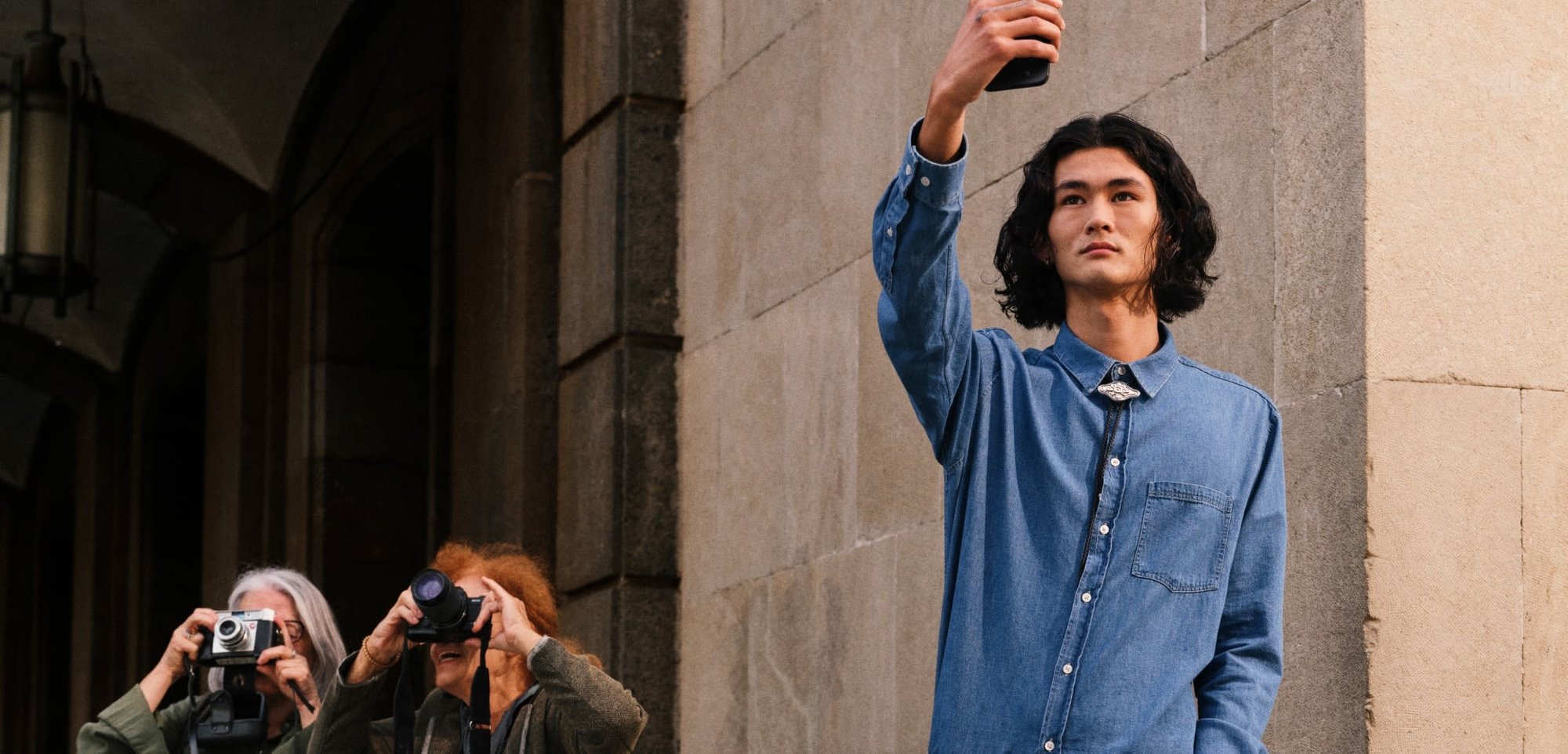 Gaiša zila džinsa krekls ar garām piedurknēm, ar vienu krūšu kabatu. Nēsāts ar pelēkiem džinsiem un melno jostu ar zelta metāla sprādzi.