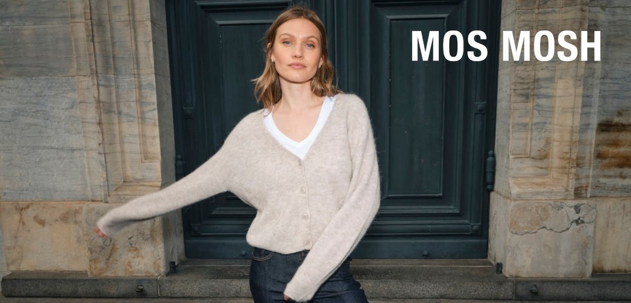 Beige knitted cardigan with a relaxed fit, v-neck, and button front. Worn over a white t-shirt, paired with dark denim jeans.