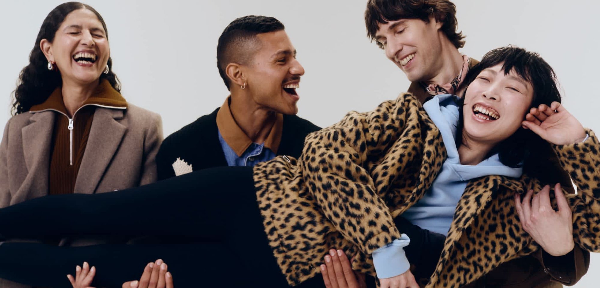 Leopard-print faux fur jacket, light blue hoodie, black leggings, with three individuals laughing and interacting against a neutral background.