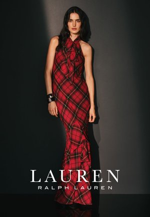 Punainen ruudullinen hihaton mekko, jossa on rusetti kaula-aukossa, liehukehelma ja röyhelöyksityiskohta alaosassa. Materiaali näyttää sileältä.