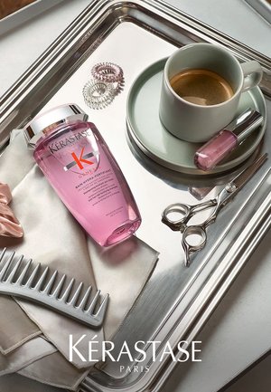 Kérastase pink Shampooflasche, silberner Kamm, Strass-Haargummis, graue Kaffeetasse auf einem hellgrauen Teller, rosa Nagellack, Schere auf einem Tablett.