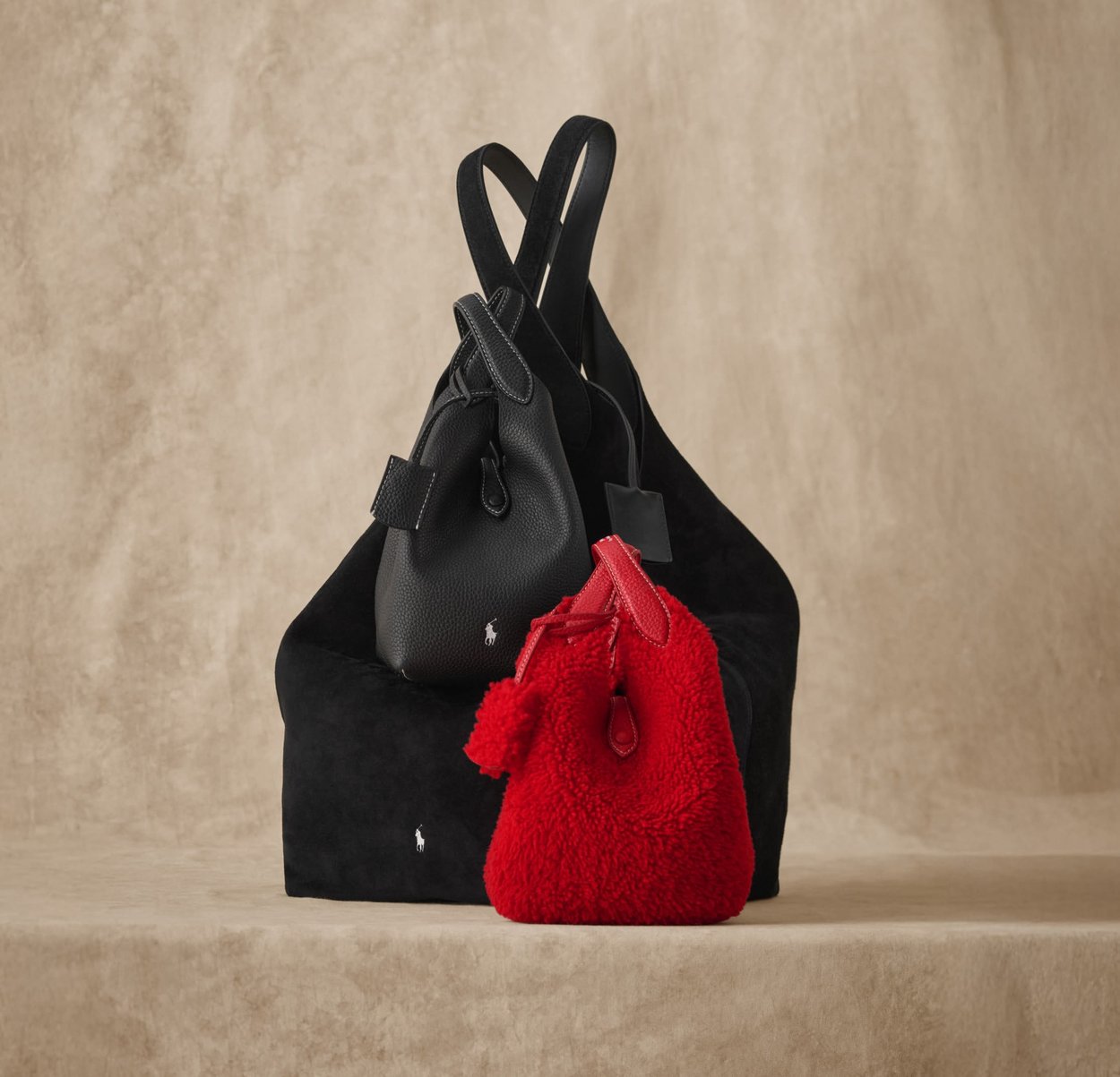 Due borse: una borsa strutturata in pelle nera e una piccola borsa di peluche rossa con una pom-pom. Entrambe presentano i loghi del brand e accessori semplici ed eleganti.