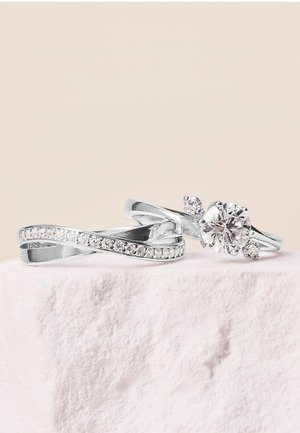 Deux bagues en argent : l'une avec un design ondulé et des pierres claires, l'autre présentant une grosse pierre centrale accompagnée de petites pierres d'accent.