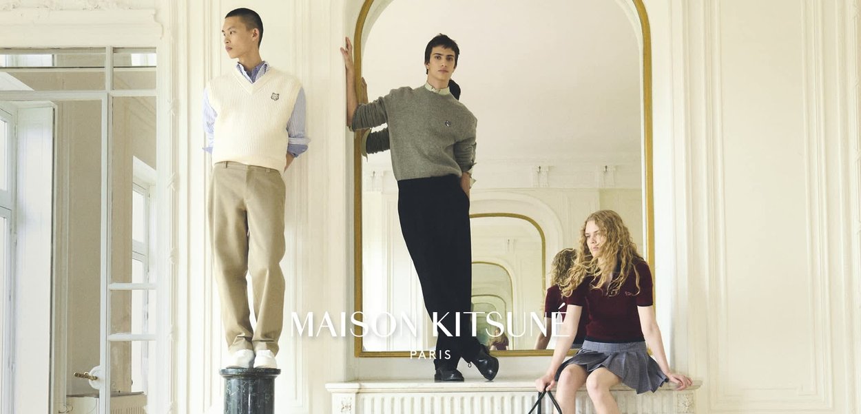 Drei junge Models posieren drinnen: eines steht auf einem Podest, ein anderes lehnt sich an einen großen Spiegel, und das dritte sitzt auf einer Ablage.