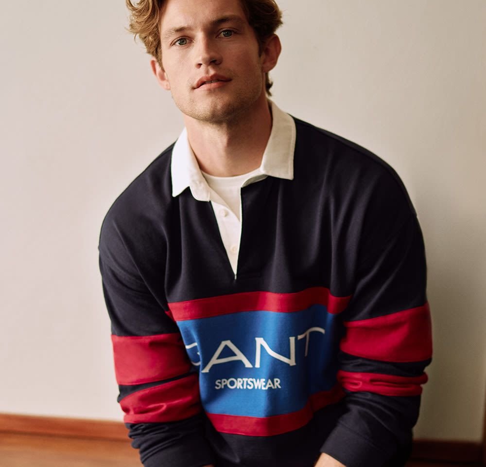 Navy and red rugby shirt with a white collar; features a large blue logo with "GANT" and "SPORTSWEAR" text, made of cotton fabric.