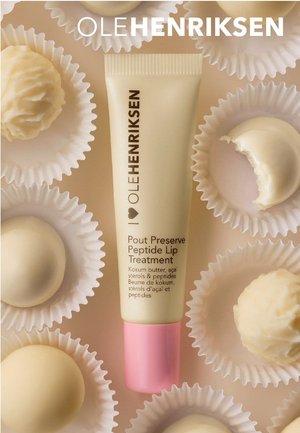 Tube de traitement pour les lèvres avec un corps beige et un capuchon rose, placé parmi des confiseries blanches ressemblant à du chocolat dans des caissettes festonnées.