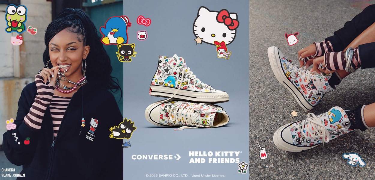 Mujer con sudadera negra y mangas a rayas modela zapatillas Converse blancas de caña alta con diseños coloridos de Hello Kitty y sus amigos, atadas sobre asfalto.