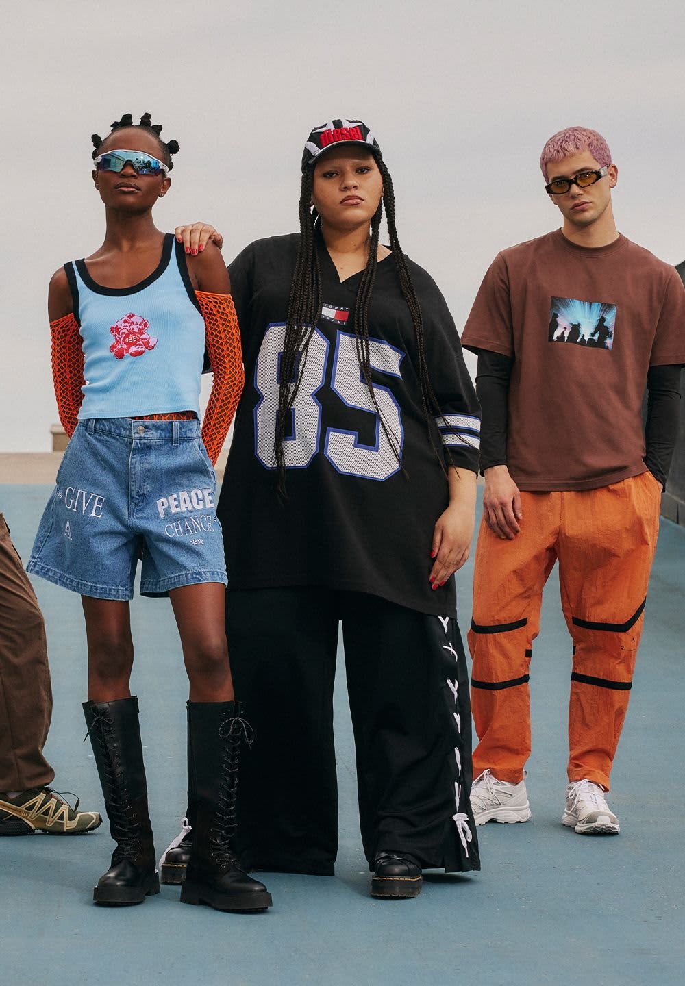 Quatre individus en tenue urbaine : shorts en denim, t-shirts graphiques surdimensionnés, pantalons cargo orange et bottes de combat, présentant des couleurs vives et des styles divers.