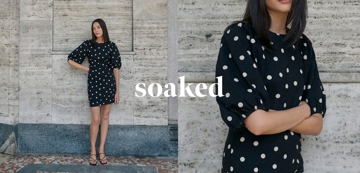 Black polka-dot dress featuring puffed sleeves, a fitted waist, and knee-length hem, set against a textured stone background.