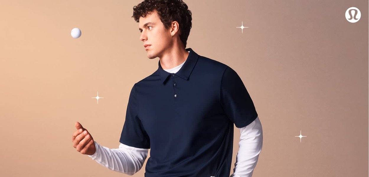Marineblaues Poloshirt mit einer Zwei-Knopf-Leiste, kombiniert mit einem weißen Langarmshirt darunter, hält einen Golfball vor einem sanften Hintergrund.