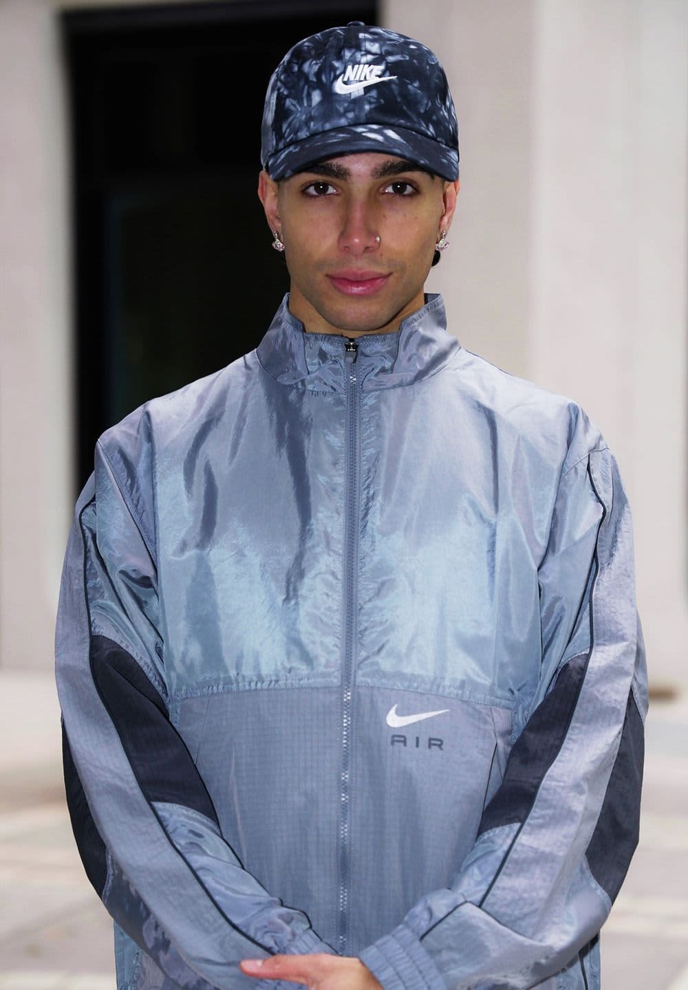 Gray Nike windbreaker jacket with dark gray accents, front zipper, and logo detail. Model wears a matching tie-dye cap.
