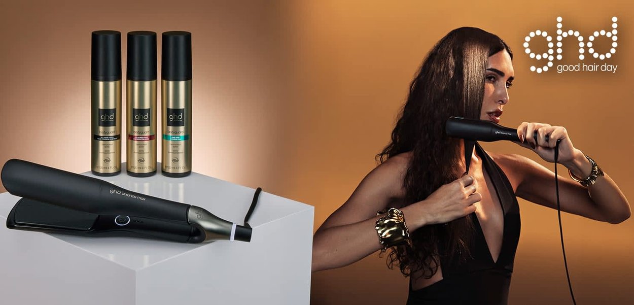 Lisseur GHD noir au design élégant, à côté de trois flacons dorés de produits coiffants. Le fond présente un dégradé chaud.