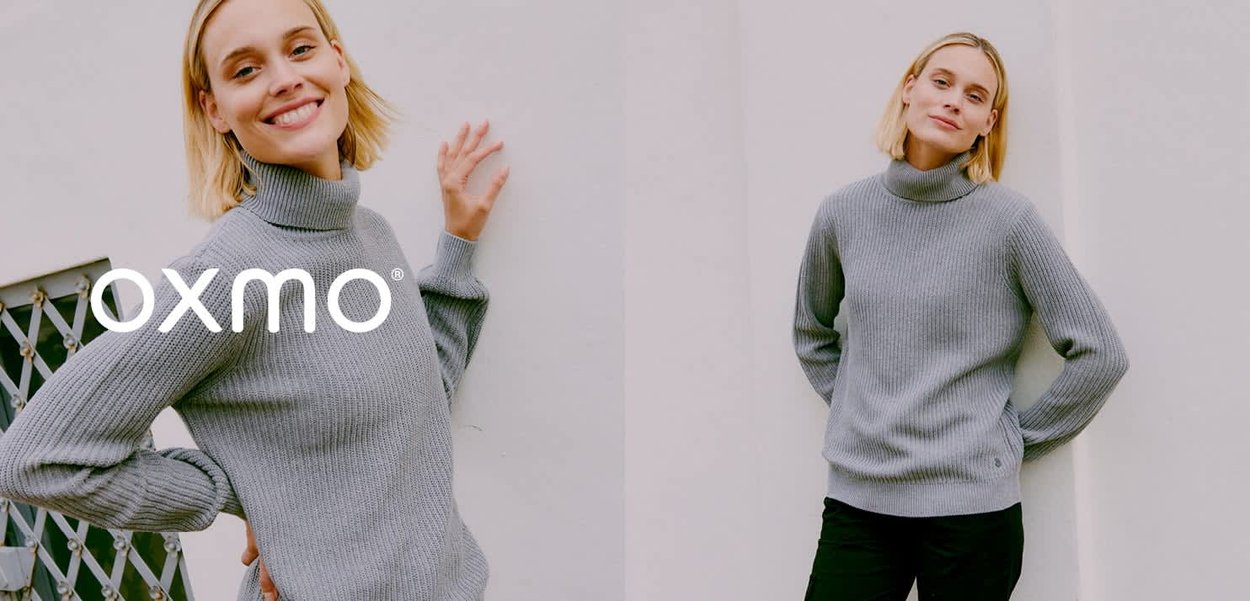 Pull à col roulé côtelé gris clair avec manches longues et coupe décontractée. Texture notable et logo de la marque à l'ourlet. Associé à un pantalon noir.