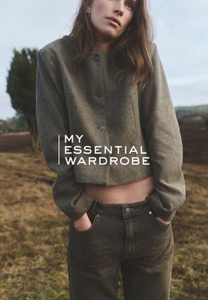 Veste en laine vert olive coupée avec des boutons noirs, associée à un jean noir. Texture douce et design simple, sur fond naturel.