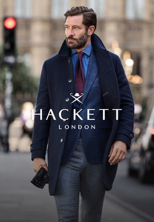 Marineblauwe wollen jas met een getailleerde pasvorm, gecombineerd met een blauw geruit gilet en lichtgrijze broek. Donkere stropdas en accessoires maken de look compleet.