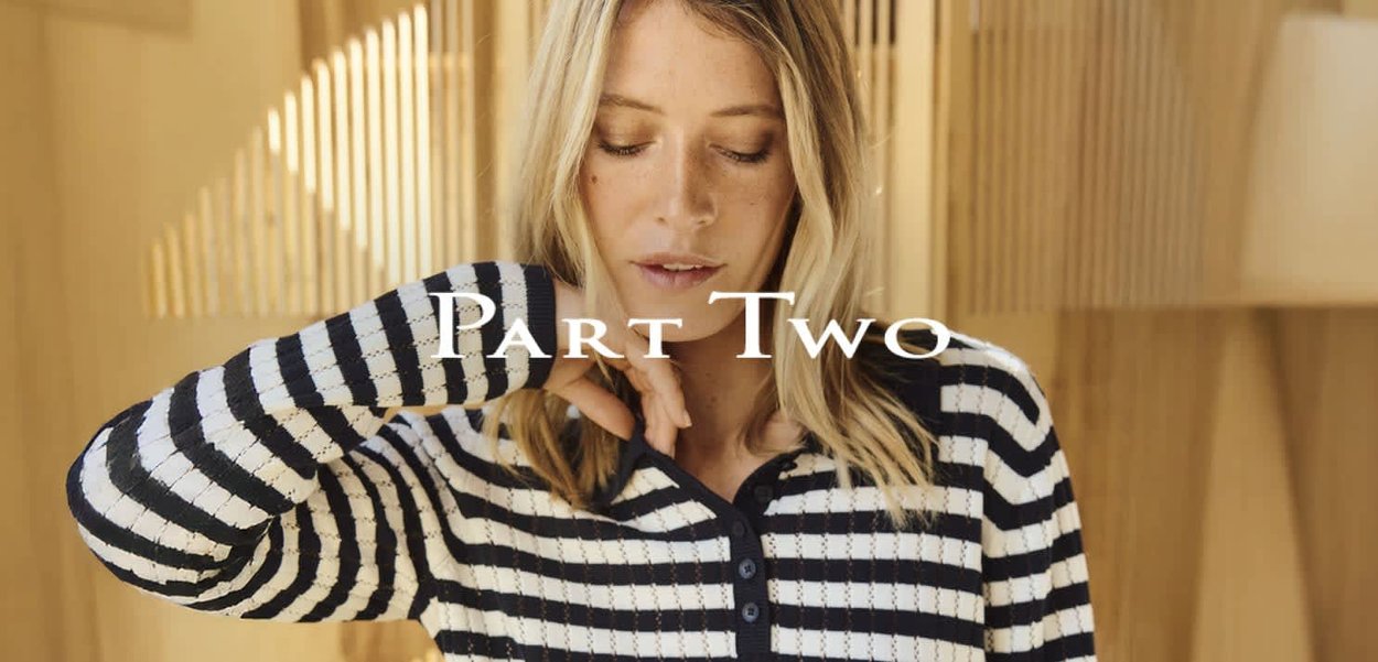 Schwarz-weiß gestreifter, gerippter Strickpullover mit einem knöpfbaren Ausschnitt. Das Modell richtet in einem hellen, sanft beleuchteten Umfeld den Ärmel.