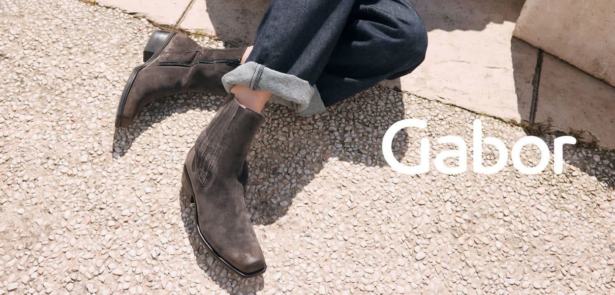Dark grey suede ankle boots with a streamlined shape, side zip, and distinct stitching details, paired with rolled-up denim.