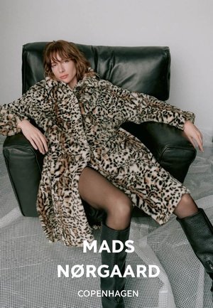 Leopard print faux fur coat with long sleeves, textured surface; black leather armchair; model wearing thigh-high boots and sheer stockings.