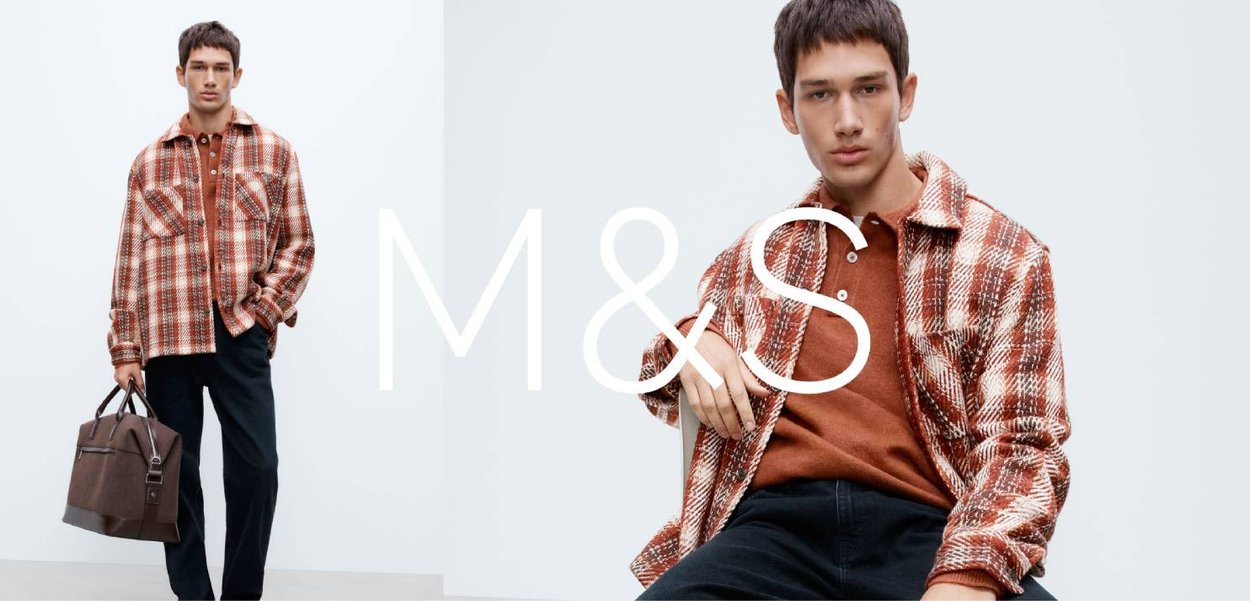 Brązowa koszula flanelowa w kratę z dwoma kieszeniami na piersi, noszona na terakotowej koszulce polo. Czarne spodnie i brązowa torba dopełniają stylizację.