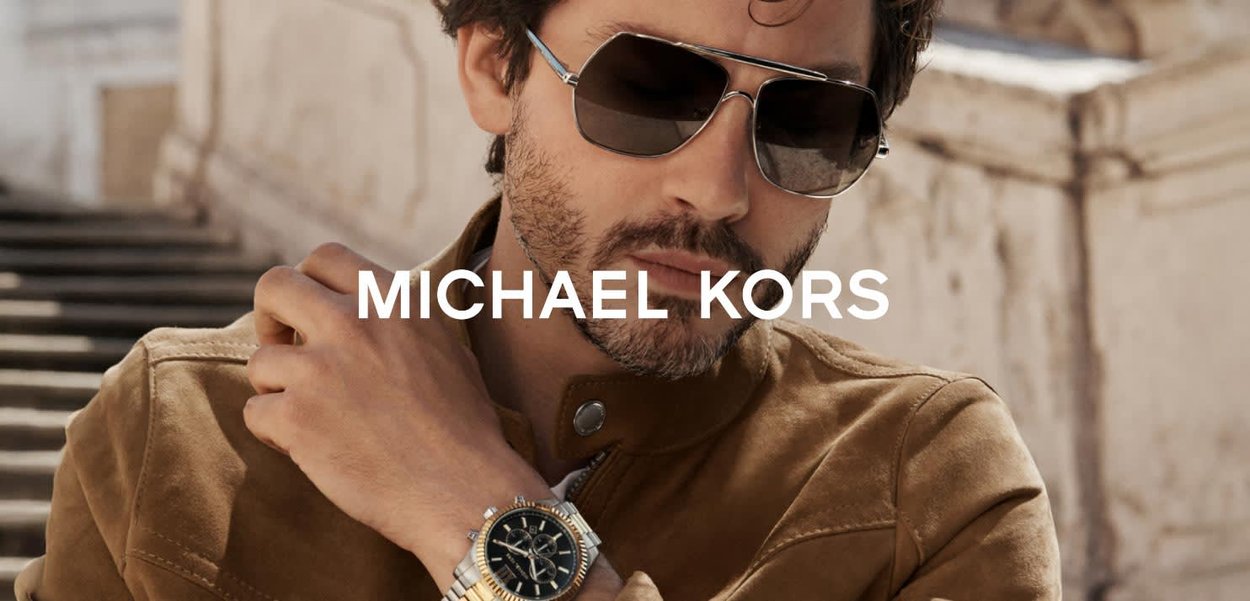 Michael Kors-solglasögon med gråa linser, silverram och en rund klocka med svart urtavla och silverdetaljer, kombinerade med en beige mockajacka.