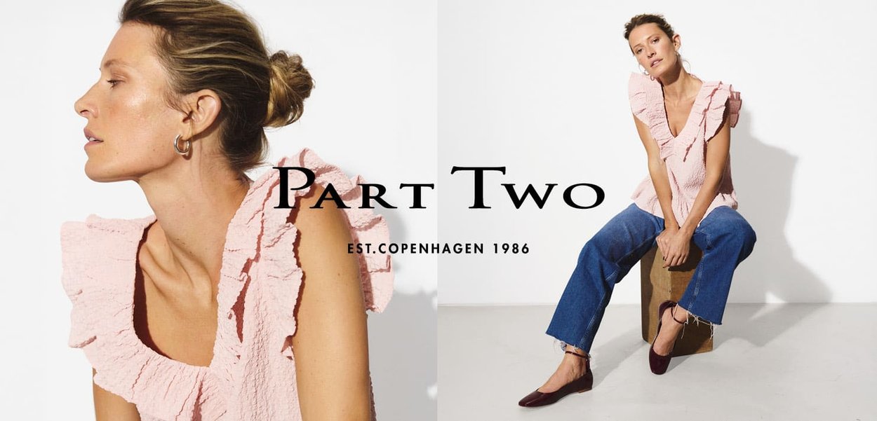 Helles rosa strukturierte Oberteil mit Rüschendetails, kombiniert mit blauen Jeans und burgunderfarbenen Schuhen. Markenname "Part Two" deutlich sichtbar.