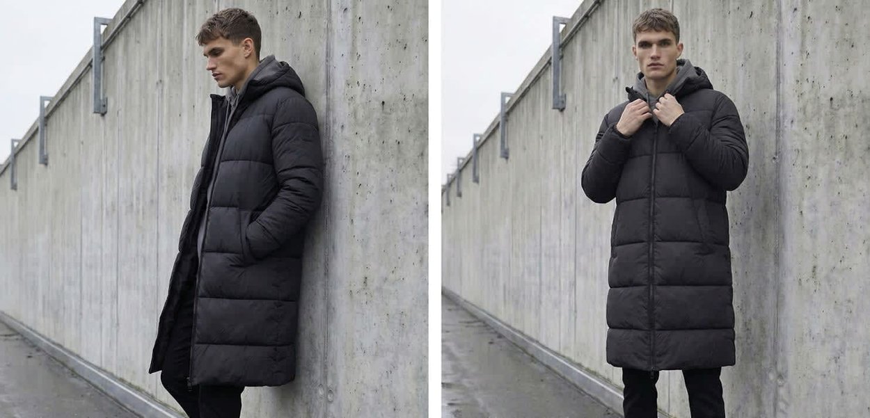 Uomo con giacca nera imbottita lunga posa davanti a un muro di cemento grigio, mostrando viste frontale e laterale in un ambiente esterno nuvoloso.
