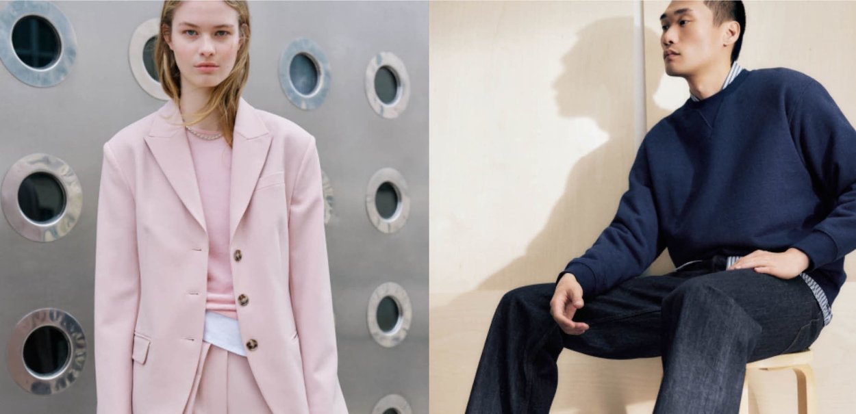 Blondynka w różowym garniturze stoi obok Azjaty, który siedzi na stołku, ubrany w granatowy sweter i ciemne spodnie, na tle jasnych ścian.