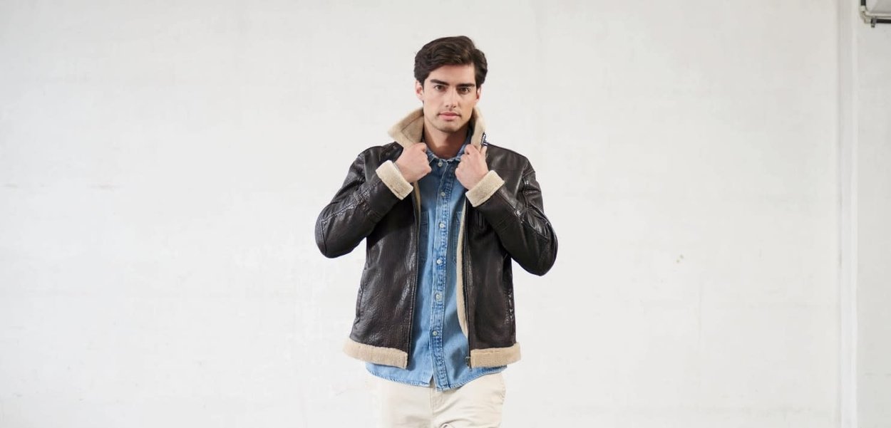 Giacca in pelle nera con colletto e polsini in shearling, caratterizzata da una chiusura con zip, indossata sopra una camicia di jeans. La modella posa davanti a uno sfondo semplice.