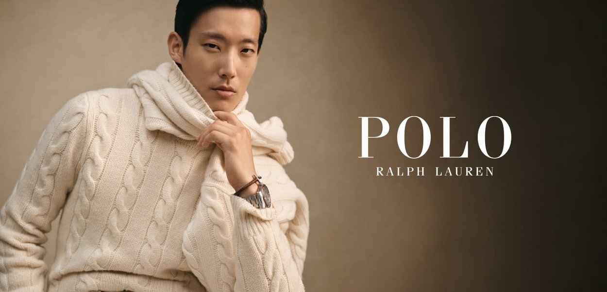 Cremefarvet cable-knit sweater med høj krave. Model poserer med armene over kors og viser et ur på håndleddet. Tekst: "POLO RALPH LAUREN."