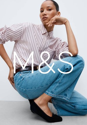 Chemise à rayures rose et blanche avec boutons, associée à un jean en denim bleu taille haute. Ballerines noires avec détail nœud. Modèle posant sur une surface grise.