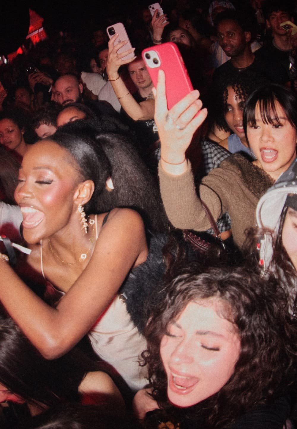 Multitud en una fiesta animada, varias personas cantando y celebrando, muchas sosteniendo teléfonos para capturar el momento.